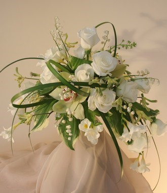 A pretty informal and delicate bridal bouquet with sweet scented lily-of-the-valley just perfect for Spring. White cymbidium orchids and snow white roses are offset with trailing lily grass.